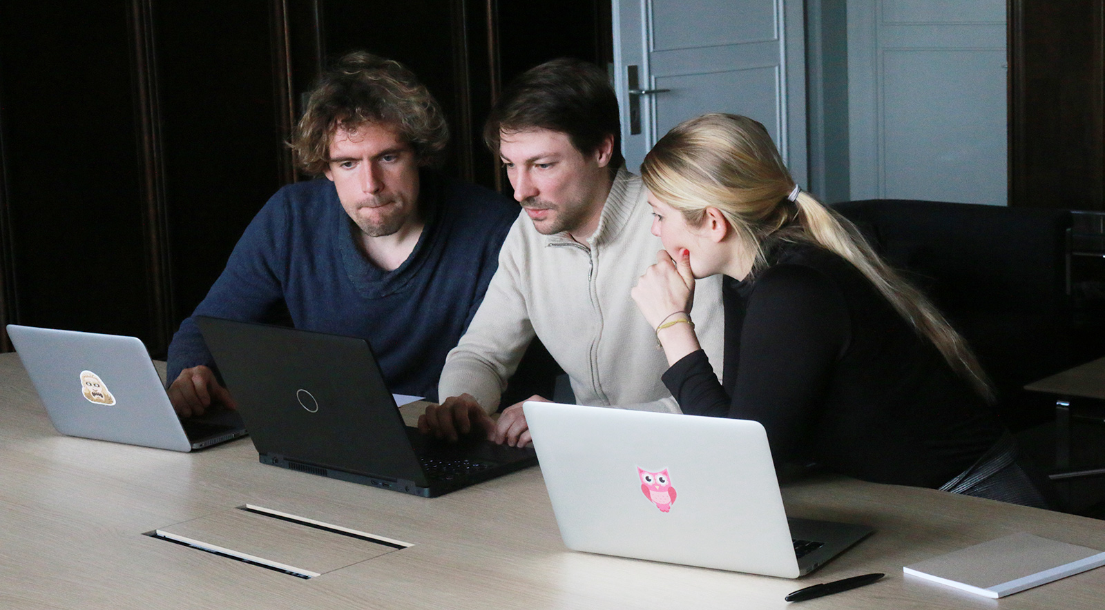 Two men and a woman sit at a table with laptops in a work situation