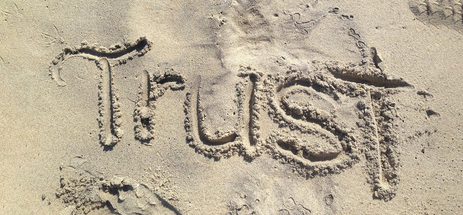 Photo of the word "Trust" written in the sand
