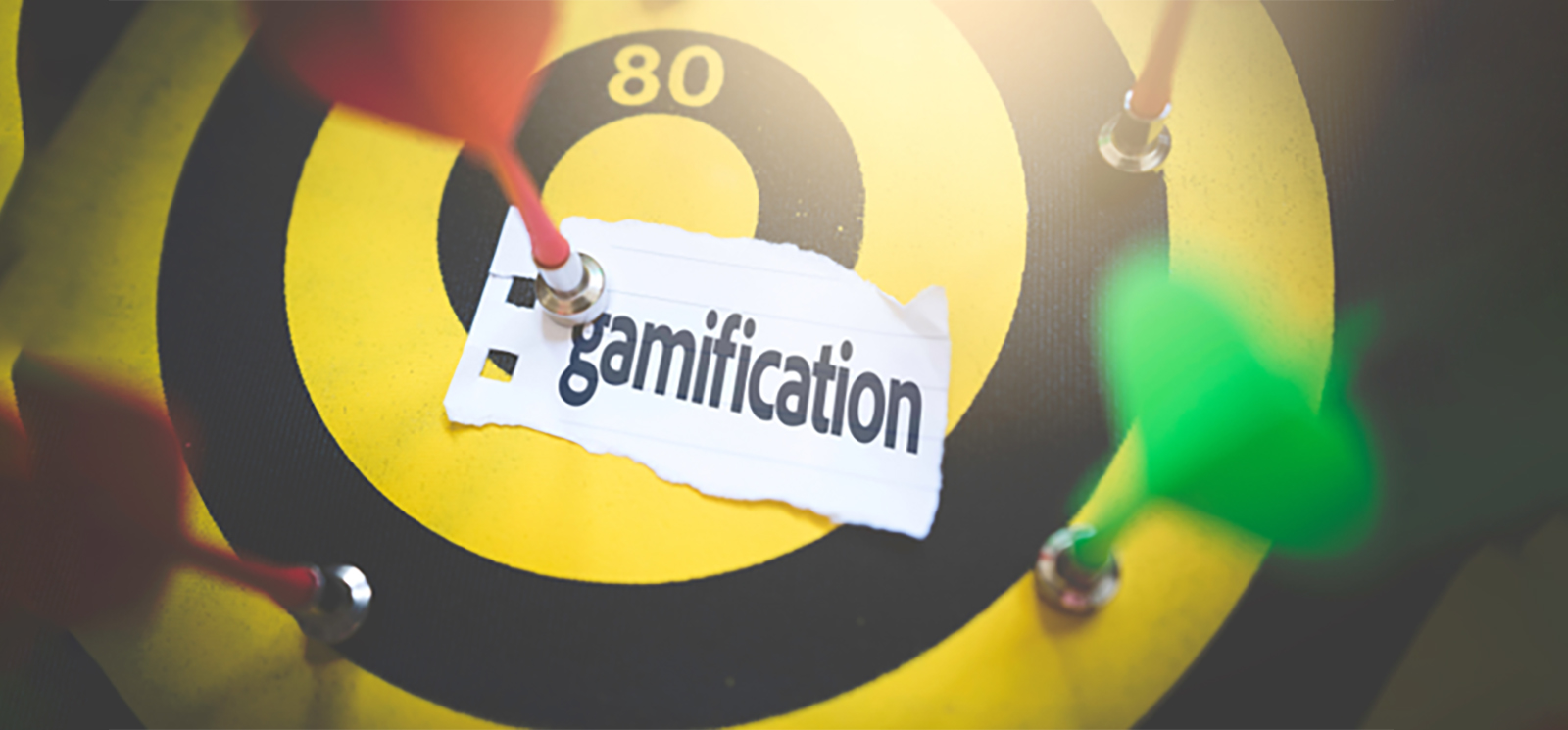 Foto einer Dartscheibe mit Pfeilen und einem Zettel, auf dem Gamification steht