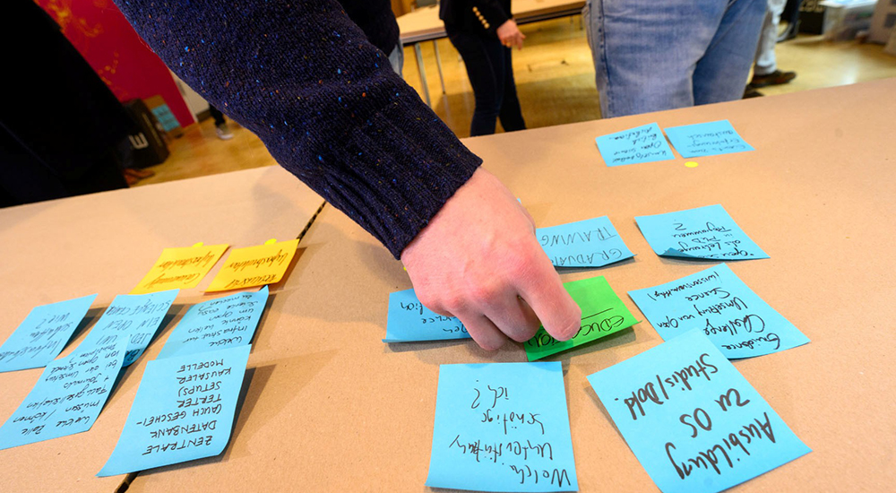 A tabletop covered in sticky notes, with a hand reaching for one.