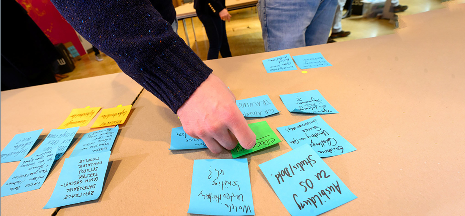 Eine Tischoberfläche auf der viele Post-its kleben mit einer Hand, die danach greift